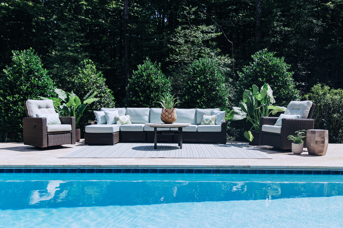 Poolside lounge seating with soft blue cushions framed by layered greenery, styled by The Open Door Style & Design · Great Falls, VA