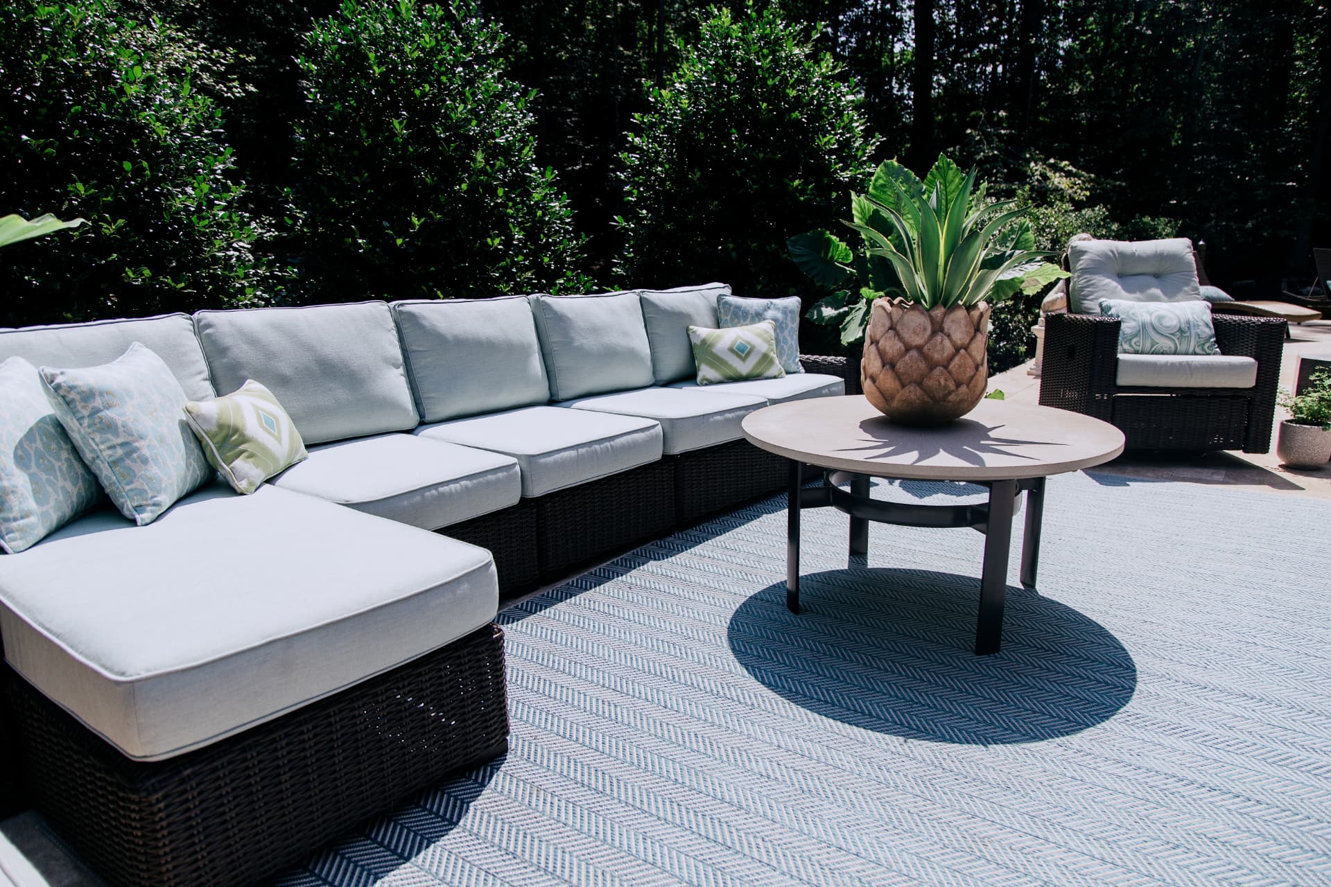 Outdoor sectional with patterned pillows and a pineapple planter on a woven area rug · Great Falls, VA